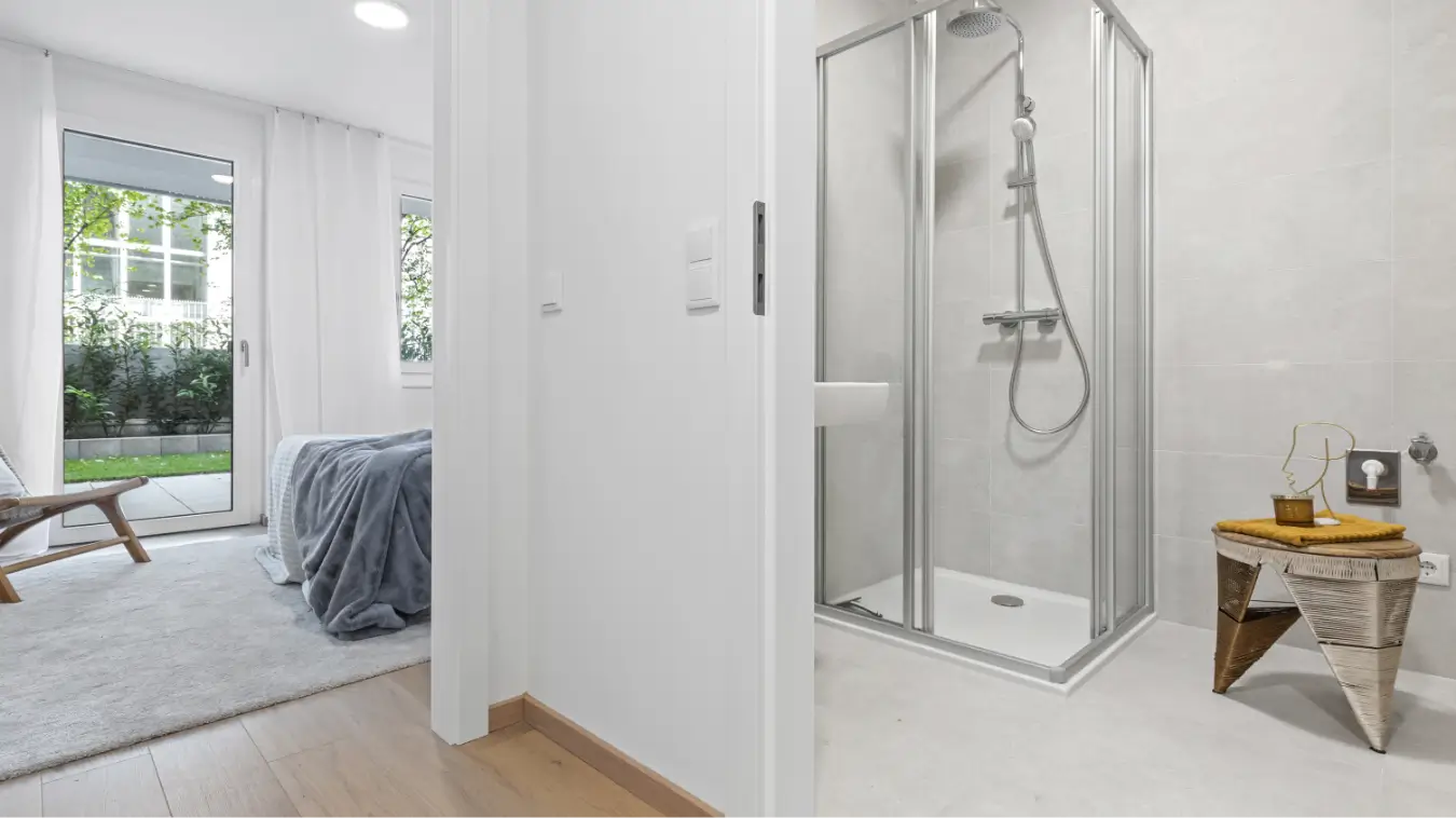 Modernes Schlafzimmer mit Holzboden und Zugang zu einem Badezimmer mit Glasdusche.