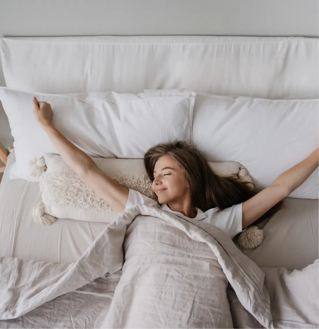 Glückliche Frau streckt sich am Morgen in einem hellen Schlafzimmer.