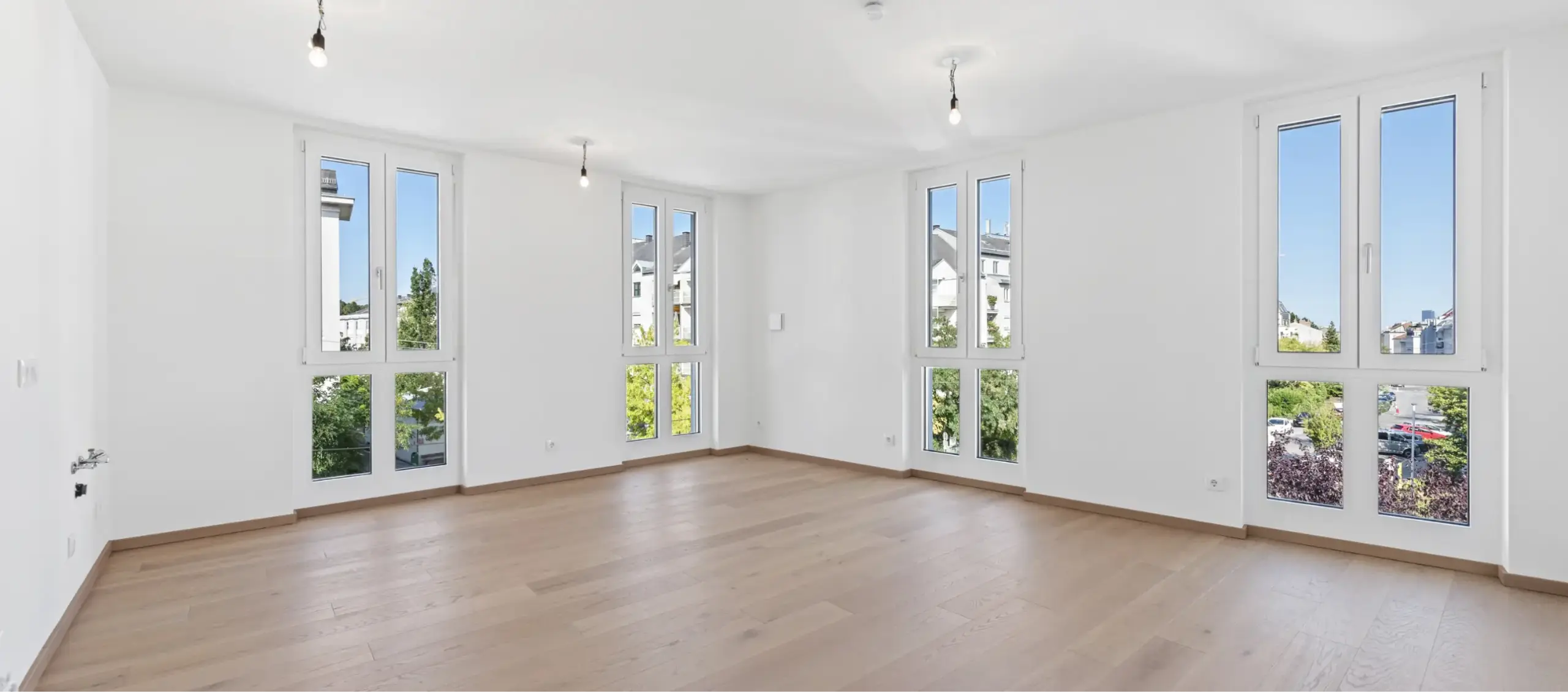 Großes, leeres Zimmer mit Holzboden und vielen Fenstern.