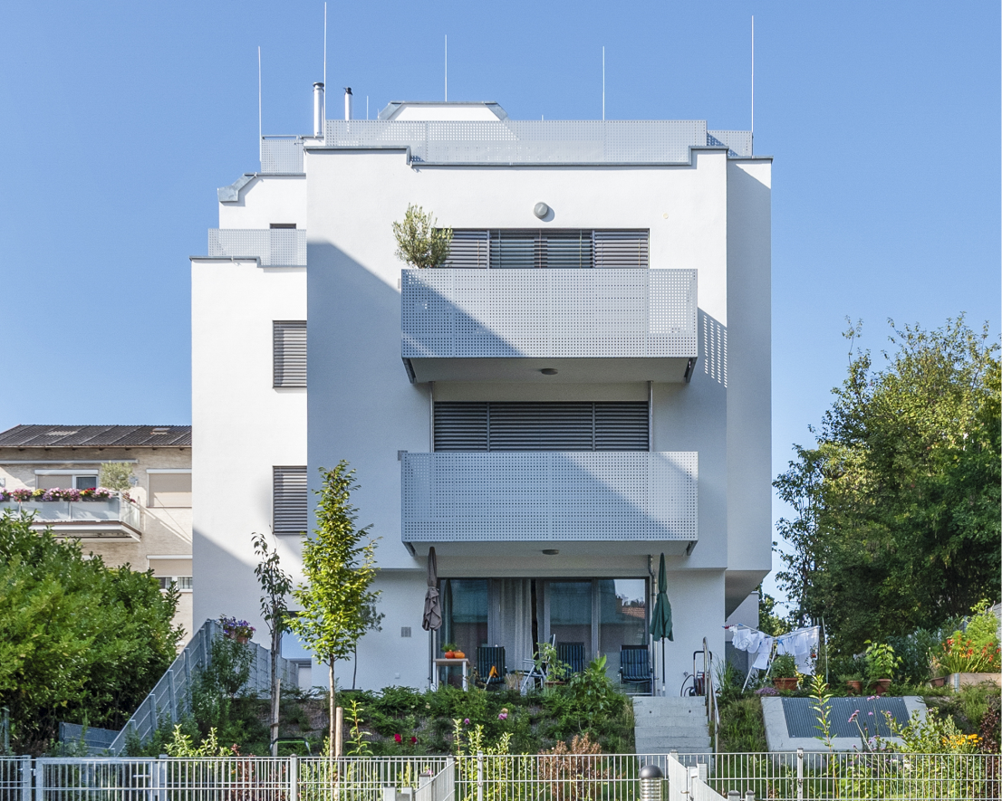 Modernes, weißes Mehrfamilienhaus mit großen Balkonen und Garten.